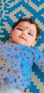 Adorable baby laying on blue patterned bedspread, smiling happily.