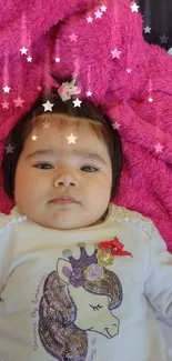 Baby lying on a pink blanket with a sweet expression, wearing a unicorn shirt.