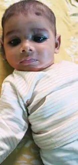 Adorable baby lying on a soft yellow bed, looking calm and serene.