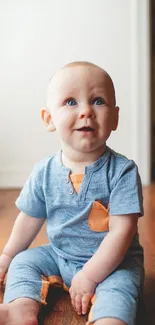 Adorable baby in blue outfit sitting on a wooden floor.