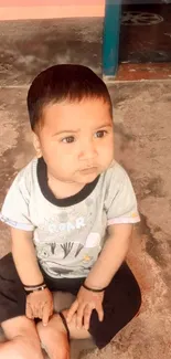 Adorable baby sitting with thoughtful expression on a warm-toned floor.