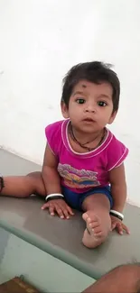 Adorable baby sitting on a bench in a pink and blue outfit.