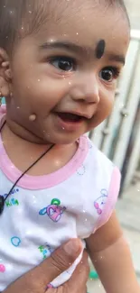 Adorable baby smiling, wearing white outfit and necklace.