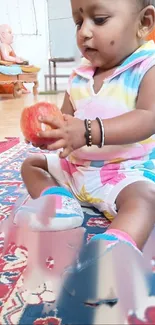 Adorable baby holding an apple on a colorful carpet.