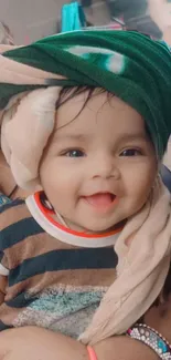 Smiling baby in striped shirt with a green blanket wrapped around.