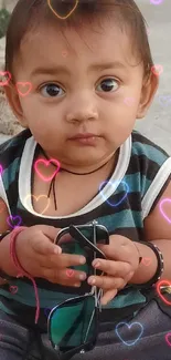 Adorable baby holding sunglasses, sitting outside.