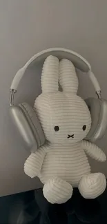 Cute white plush bunny with silver headphones on a gray background.