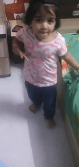 A little girl standing beside a bed in a cozy bedroom.