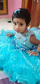 Child in a sparkling blue dress sitting indoors.