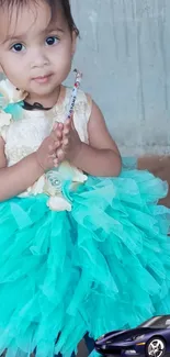 Adorable toddler in a turquoise ruffle dress with intricate floral designs.