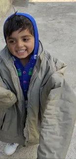 Child smiling in oversized gray coat.