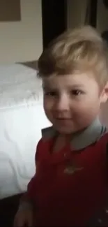 Adorable child in a red shirt smiling indoors.