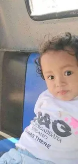 Cute child sitting with a smile, wearing a graphic tee.