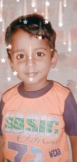 Smiling child in orange shirt against brick wall.