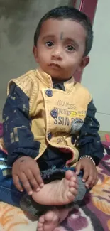 An adorable young child sitting on a colorful blanket.