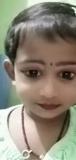 Charming child with big eyes and bindi in green attire.