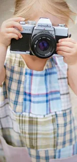 Child wearing plaid dress holding vintage camera.