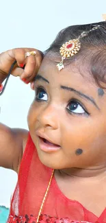 Adorable child in red attire with traditional jewelry and bright eyes.