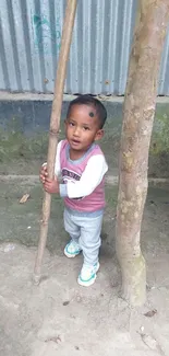 Adorable child standing with bamboo and tree in a serene outdoor setting.