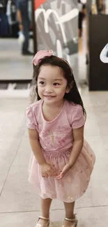 Adorable young girl in a pink dress, smiling indoors.