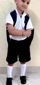 Cute child in school uniform standing against a beige wall.