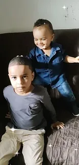 Two happy kids sitting on a dark sofa indoors.