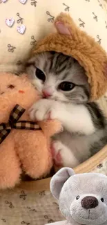 Kitten in bear hat hugging a soft toy.