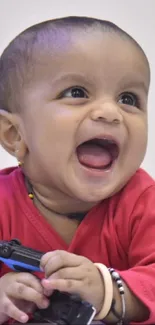 Adorable baby laughing in a red sweater, holding a toy.