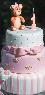 Pink birthday cake with bear topper and candle.