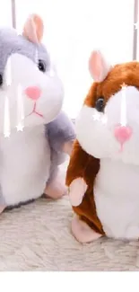 Two adorable plush hamsters in brown and grey, sitting on a soft surface.