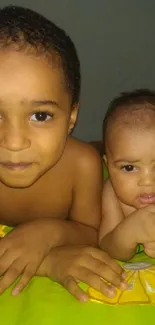 Adorable siblings lying on green background, smiling at camera.