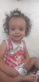 Smiling baby in a cute outfit sitting indoors.