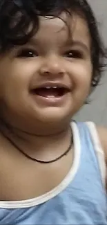 Adorable baby in blue tank top smiling joyfully.