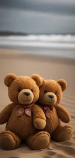 Two teddy bears sitting on a sandy beach by the ocean.