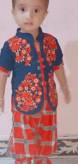 Toddler standing in colorful traditional outfit against a light pink background.