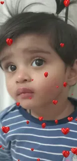 Cute toddler with playful hair in a blue striped shirt on white wall.