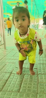 Adorable toddler stands on bright pathway under a green canopy.