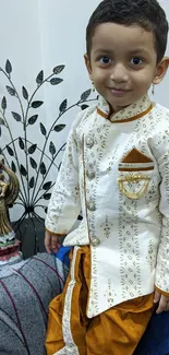 Toddler in traditional attire smiling, seated on a sofa.