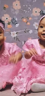 Adorable twin baby girls in pink dresses with floral background.