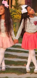 Twins in pink skirts and striped tops outdoors.