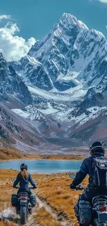 Motorcyclists ride towards snow-capped mountains under clear sky.