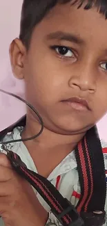 Young child holding a camera against a soft pink background.