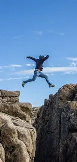 Person leaping over rocky cliffs under a clear blue sky, capturing adventure.