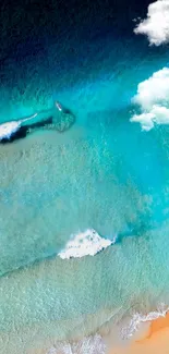 Aerial view of ocean waves and sandy beach with turquoise waters and clouds.