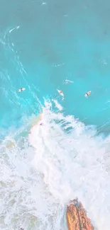 Aerial view of surfers in turquoise ocean waves and rocky beach.