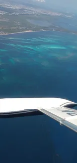 Aerial view of ocean and coastline from a plane wing, showcasing vibrant blue waters.