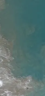 Aerial view of ocean waves and sandy beach with teal blue water.