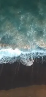 Aerial view of ocean waves crashing on a dark sandy beach shore.