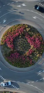 Aerial view of a roundabout with vibrant pink flowers and traffic.