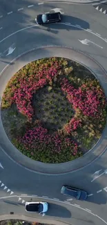 Aerial view of a roundabout with vibrant flowers and moving cars.